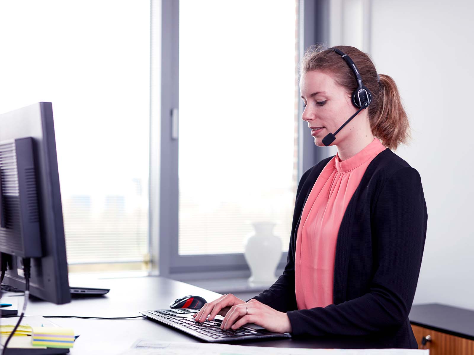 Kvindelig kundeservice medarbejder står ved pc med headset på.